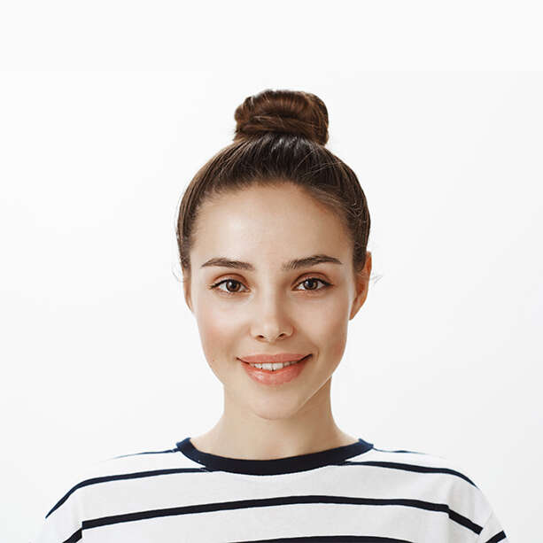 Attractive sensual woman knows how to achieve her goal. Indoor shot of positive good-looking feminine girl with bun hairstyle, smiling flirty while talking with coworker she likes over white wall.